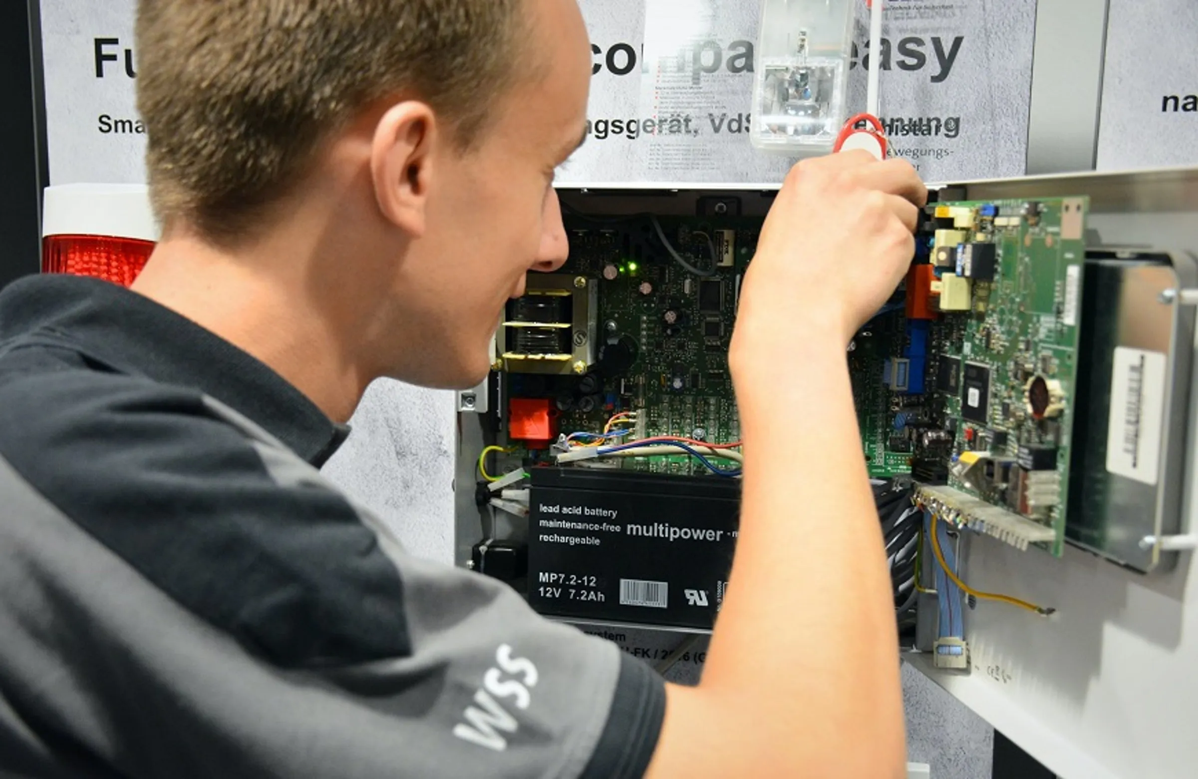Techniker montiert eine Platine in einer elektronischen Steuerung, Multiground-Batterie sichtbar.